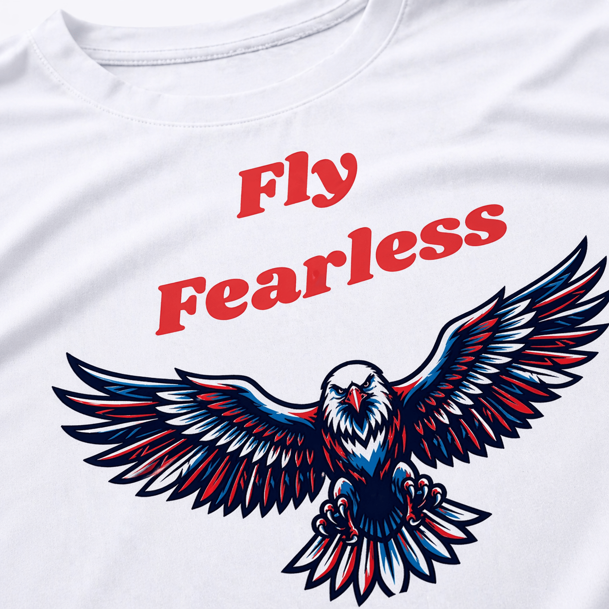 Close-up of Fly Fearless eagle wings graphic print in blue red and black on white cotton t-shirt, bold motivational streetwear design detail